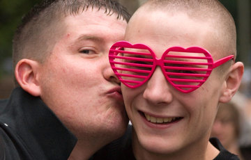 En man med rosa hjärtformade glasögon får en puss på kinden av en man.