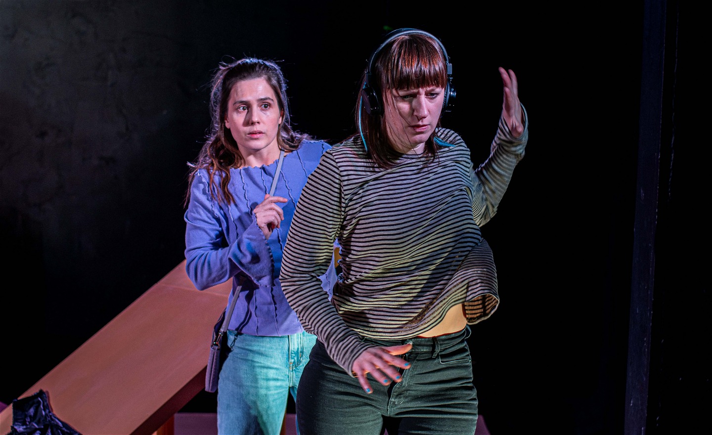 En tjej står längst fram i bilden och håller upp en avvärjande arm mot en tjej som står bakom henne. 