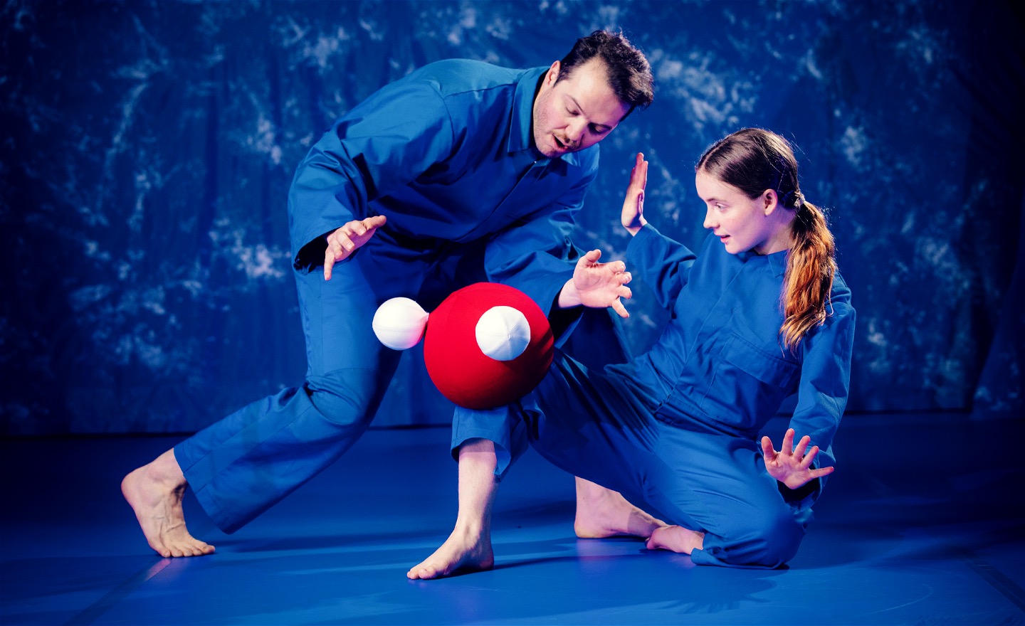 En dansare balanserar en vattenmolekyl på knät, en annan dansare tittar förundrat