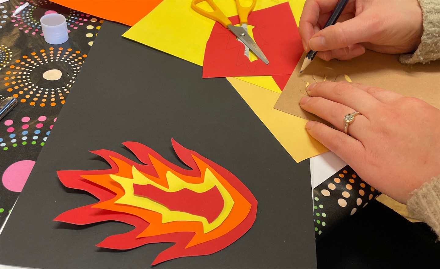 Närbild som visar papperscollage föreställande en eld med flammor mot svart bakgrund. 