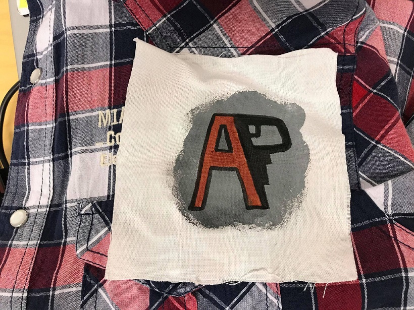 foto av en rutig skjorta med ett tygtryck som eleven gjort i syslöjden. på trycket står det bokstaven a. bokstaven har en pistol som siluett.