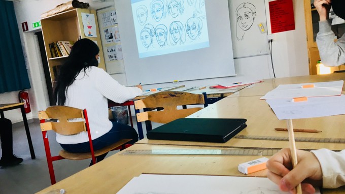 Tecknade ansikten projiceras på tavlan i ett klassrum samt elever som tecknar.