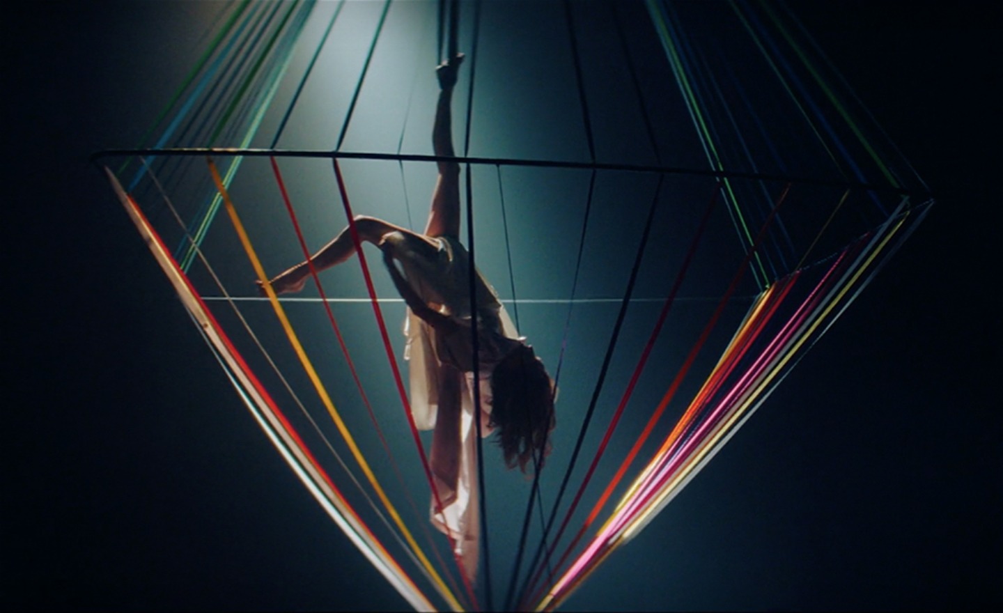 Diamont of Colourful strings with a circus artist hanging from one foot