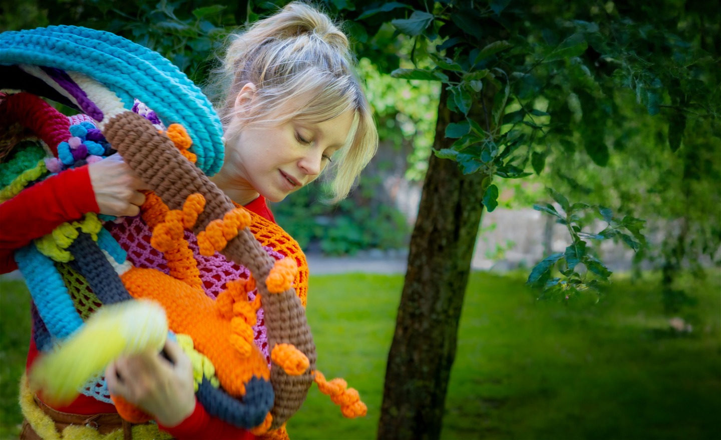 Anna dansar ute i en park, hon har famnen full av färglada virkade ormar och Virklingar