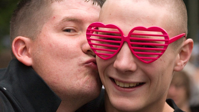 En man med rosa hjärtformade glasögon får en puss på kinden av en man.