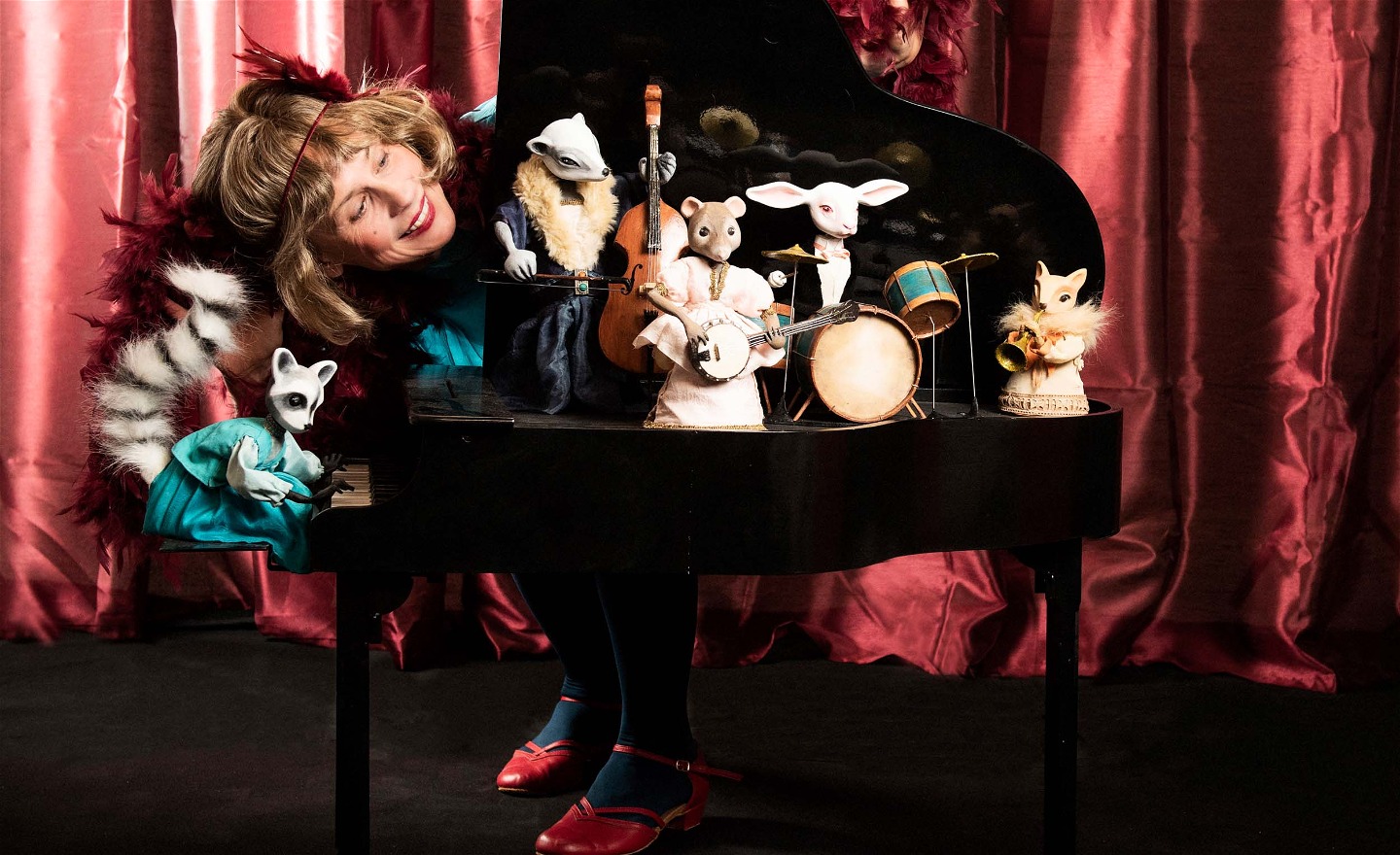 Micaela Gustafsson i turkos Charleston-outfit kikar fram bakom en liten flygel med dockdjur med instrument på