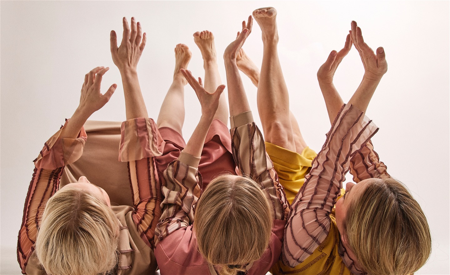 Tre dansare ligger på rygg med händer och fötter sträckta mot luften. tre huvuden närmast kameran