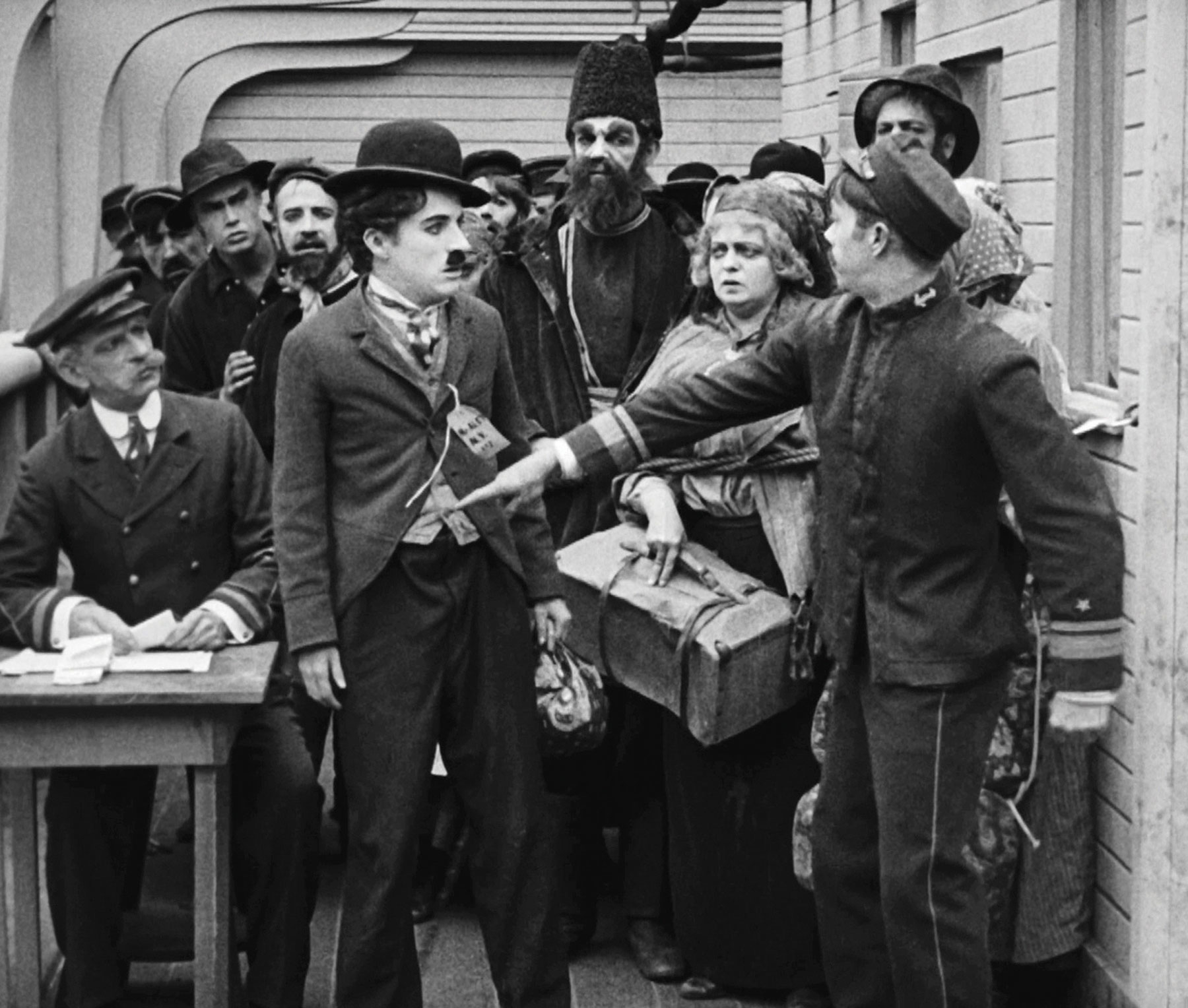 foto från filmen emigranten. charlie chaplin stoppas av en tulltjänsteman som pekar honom i magen 