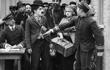 Foto från filmen Emigranten. Charlie Chaplin stoppas av en tulltjänsteman som pekar honom i magen