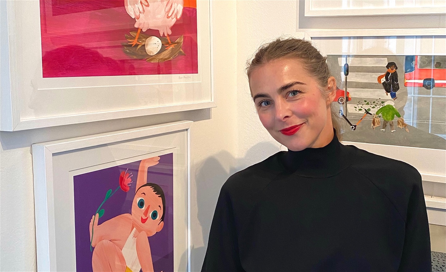 Fotografi på Hanna Albrektson tittandes emot kameran. på den vänstra sidan av bilden syns delar av två illustrationer som är från av hennes böcker. 