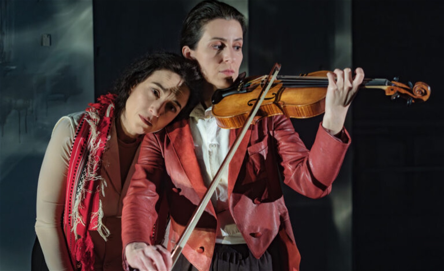 En kvinna lägger huvudet på en fiolspelande kvinnas axel.