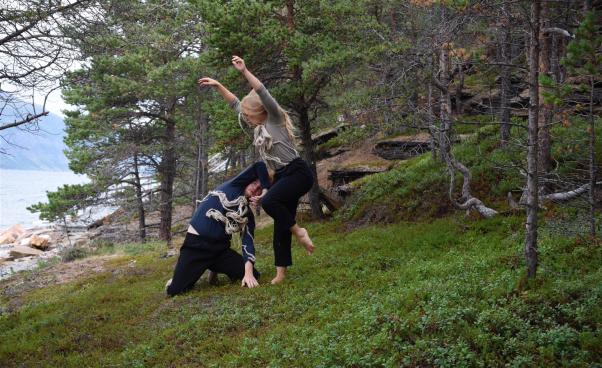 Två personer dansar barfota i skogen.