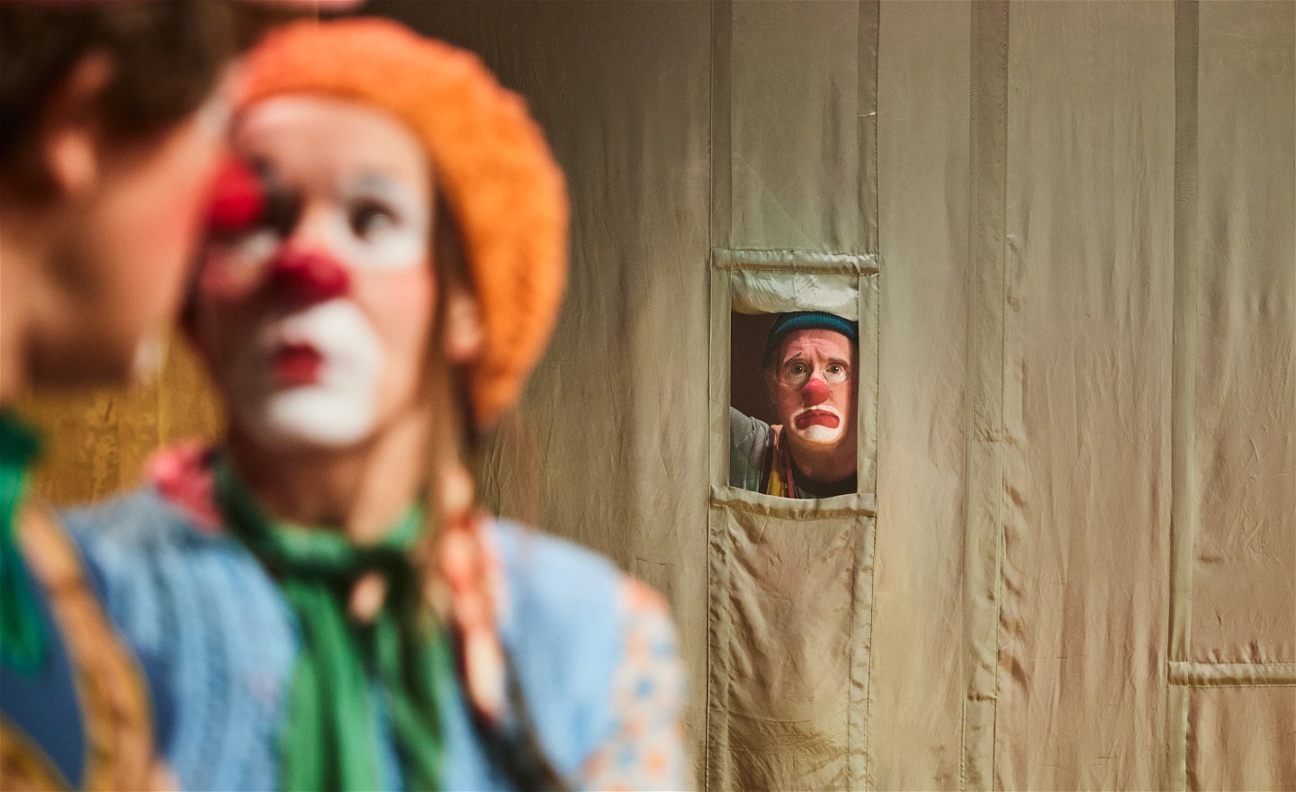 Två clowner i förgrunden suddiga, i bakgrunden en annan clown tittar ut genom en lucka 