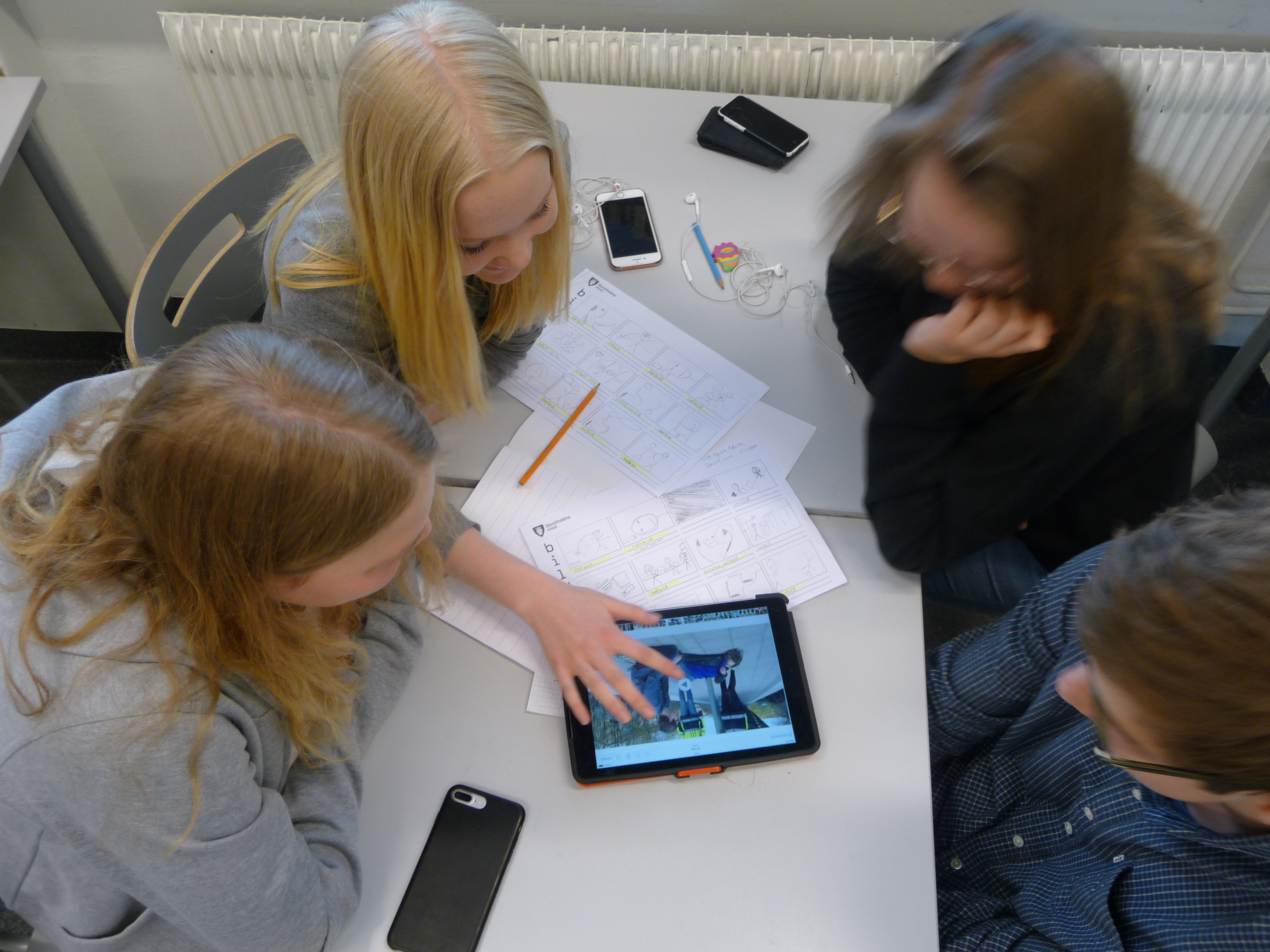 Elever sitter runt ett bord och arbetar, bildmanus och ipad sett uppifrån