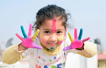 En flicka med målarfärg på händerna och i ansiktet.