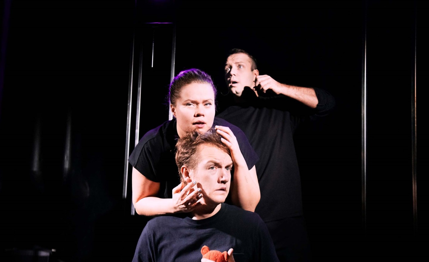 Tre personer i mörka kläder mot mörk bakgrund.