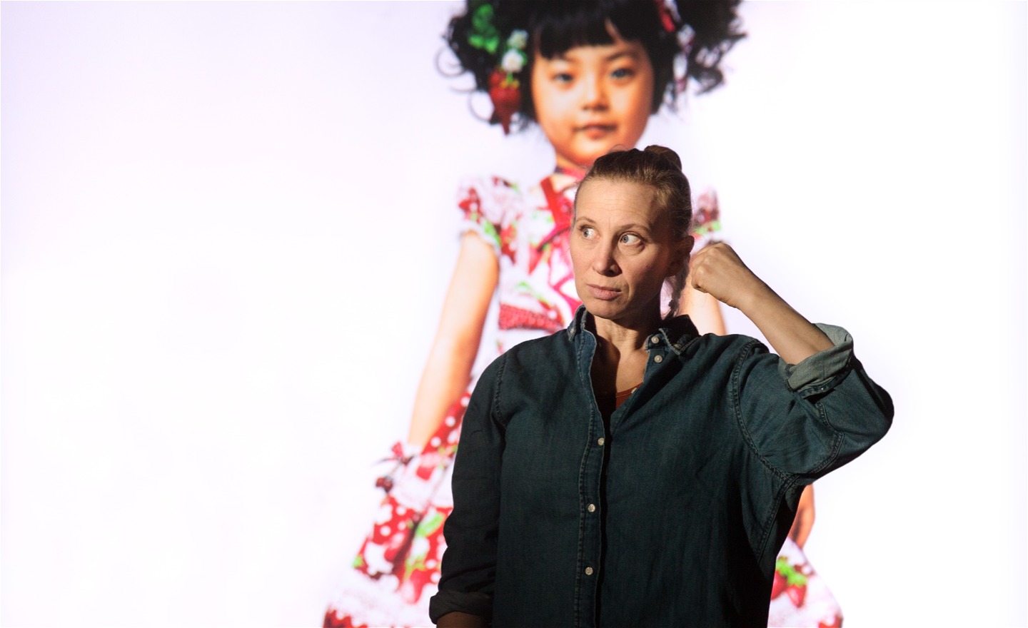 Skådespelare står framför stort foto av lite japansk flicka i jordgubbsklänning.