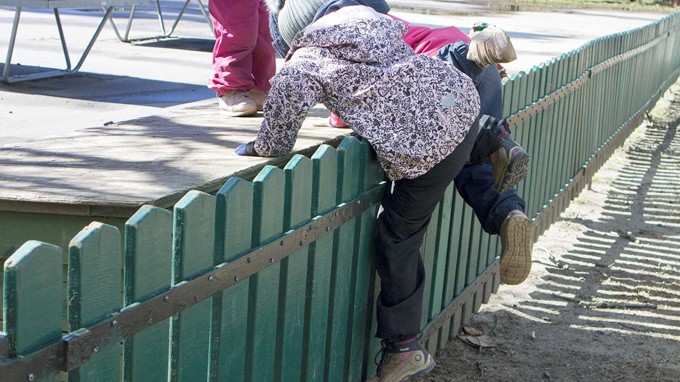 Ett barn klättrar över ett staket i lekparken.