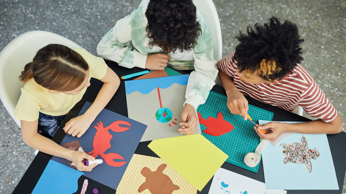 Tre personer skapar kollage med olikfärgade papper och figurer.