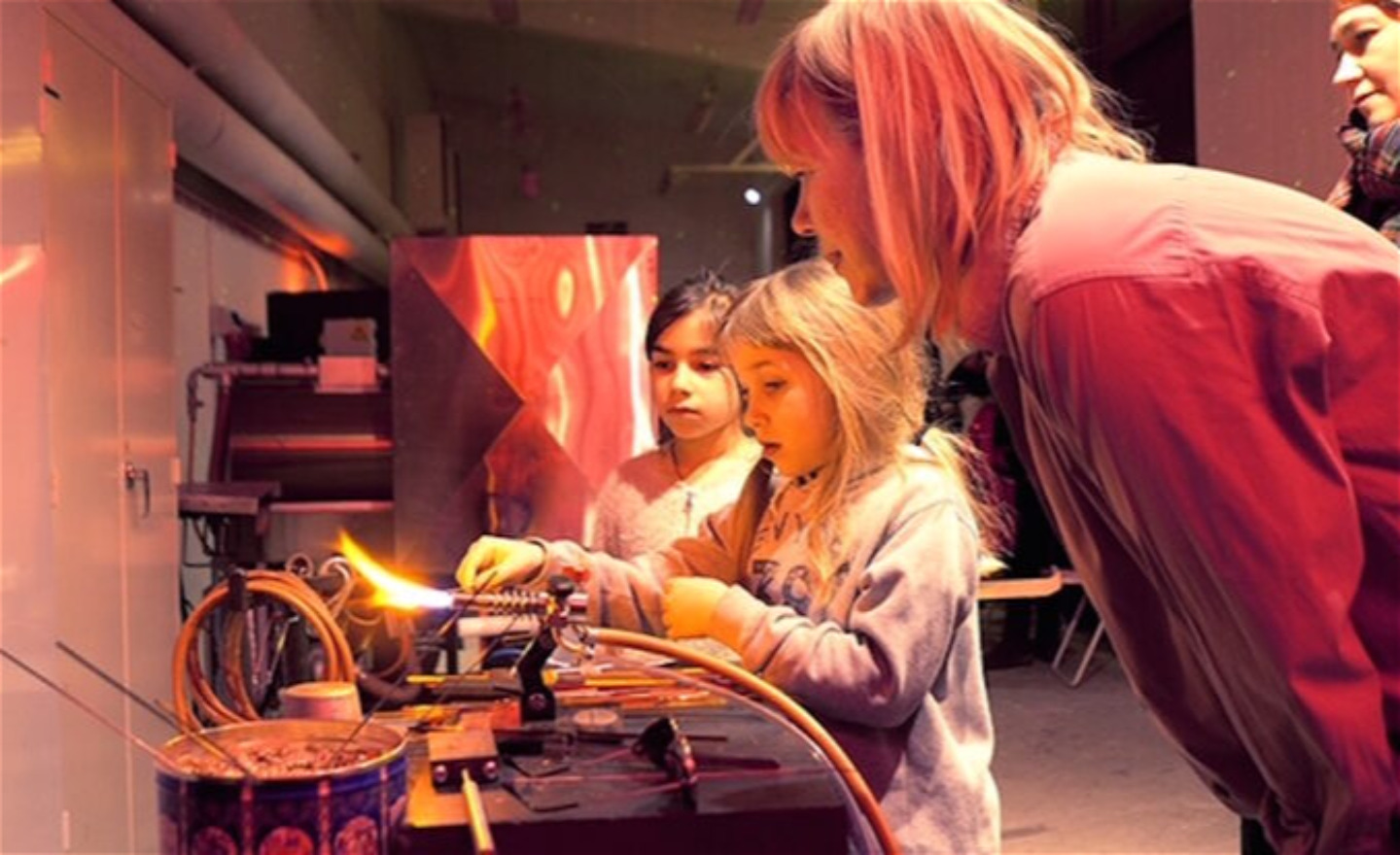 Två barn och två vuxna i en verkstad för glasblåsning.