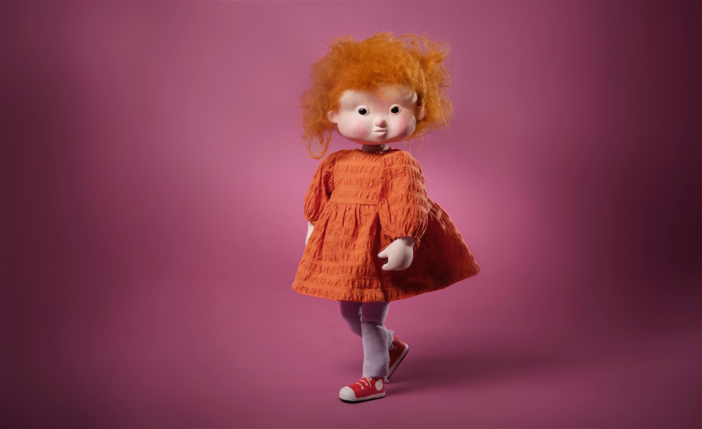 Lorpan, med rufsigt hår och orange klänning, mot en mörkt rosa bakgrund.