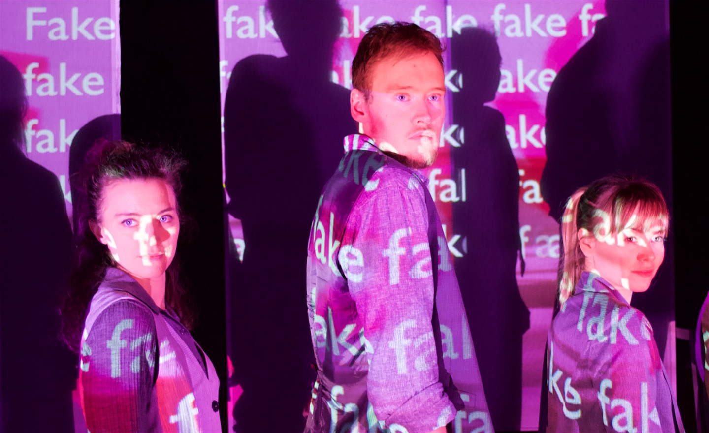 Tre dansare ser fram mot publiken täckta av projektioner med ordet 