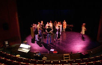 Skådespelare samlade i en cirkel på en scen sett uppifrån.