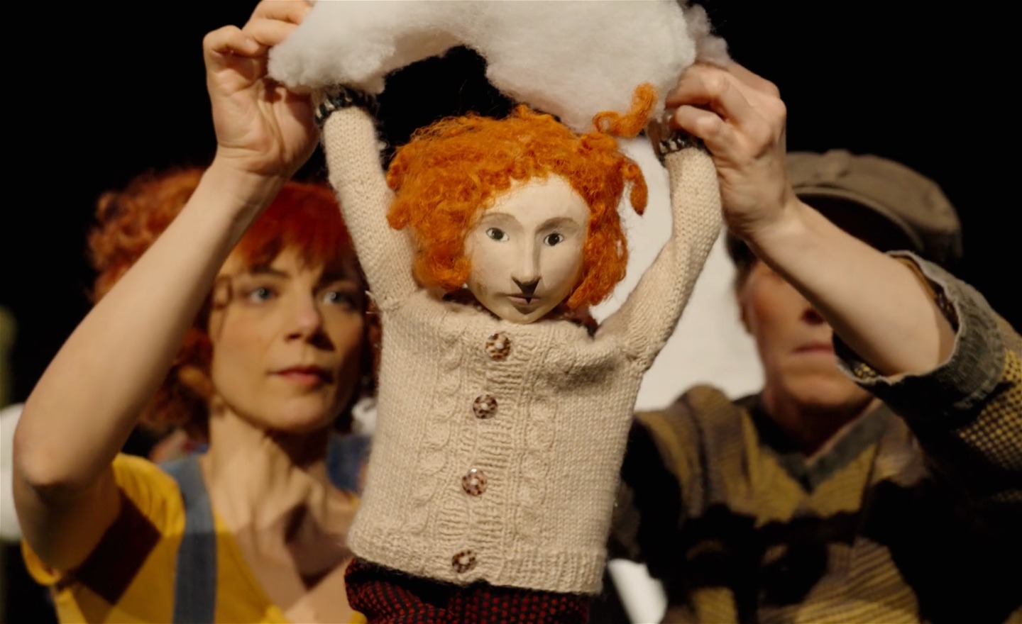 Två personer håller i en docka och ett vitt moln som dockan också håller i. 