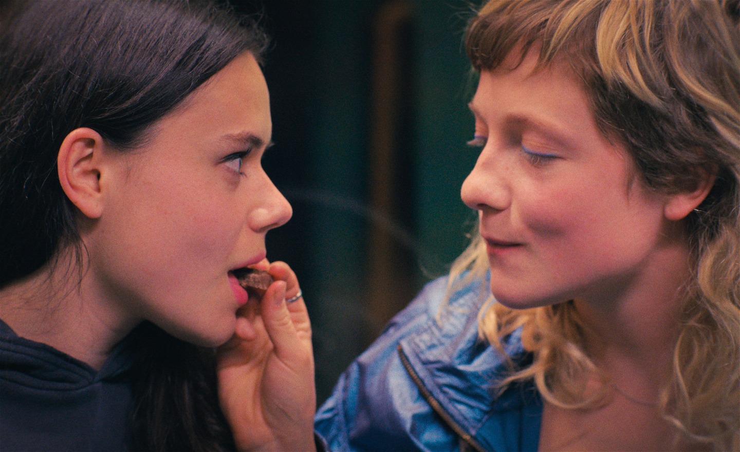 Två tonårsflickor. Den ena stoppar en chokladbit i den andres öppna mun.