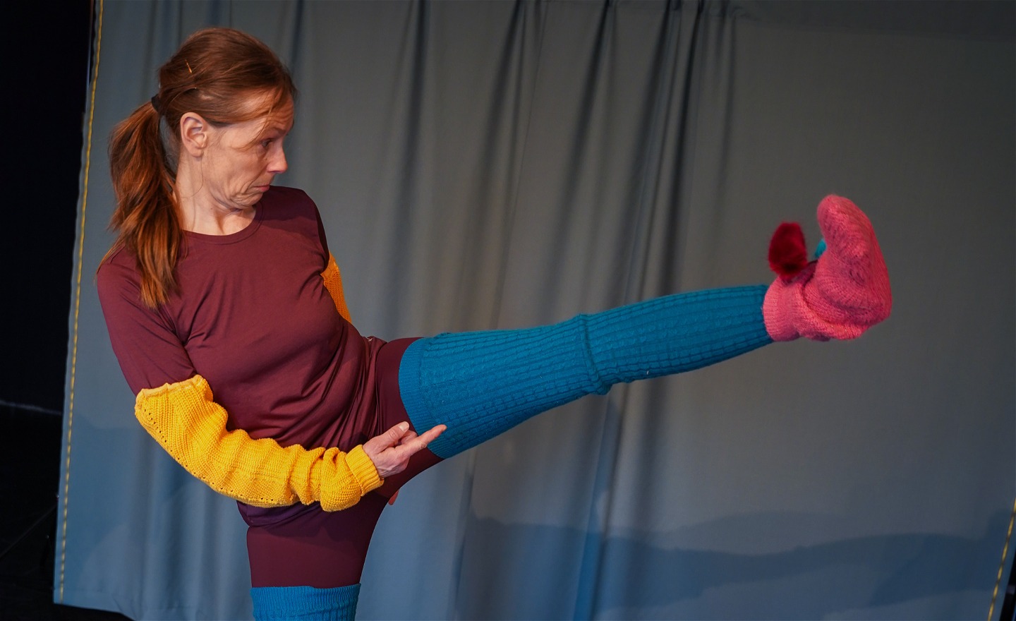 Micaela lyfter ena benet högt upp i lyften. Hon har en gul arm, blått ben och en rosa socka