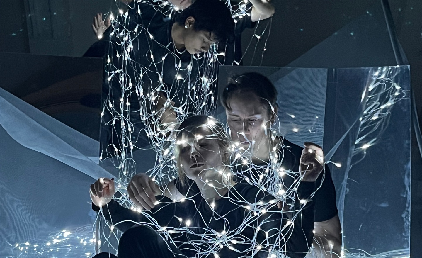 Ljusnät över 4 dansare i svarta kläder med speglar bakom