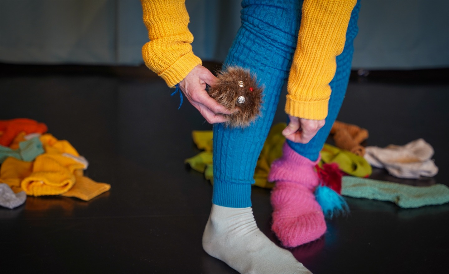 Gullig liten möss-toffs med öron näsa mun kryper på ett blått ben, man ser även en gul arm och en rosa socka