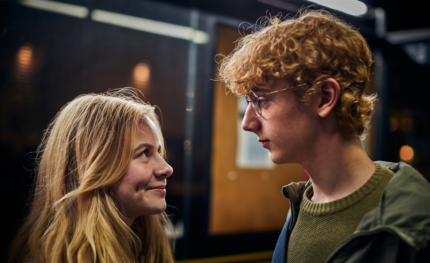 En långhårig flicka ler och tittar på Bert som står mitt emot henne och tittar tillbaka. Han ser allvarlig ut.