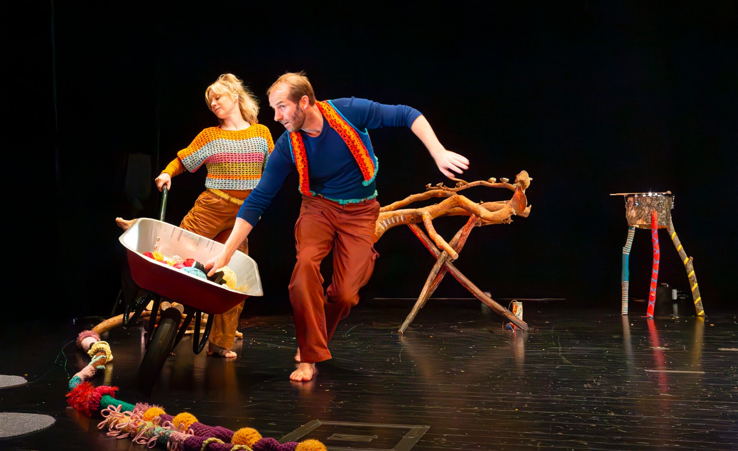 Två personer med en skottkärra. Färgglatt garn på golvet.