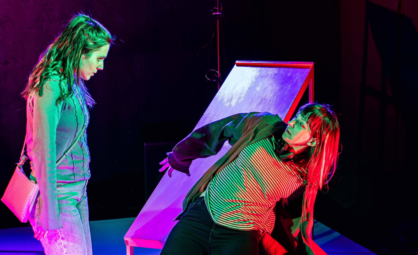 Två tjejer tittar på varandra. Den ena är bakåtböjd med kroppen och den andra tittar ner på henne. 