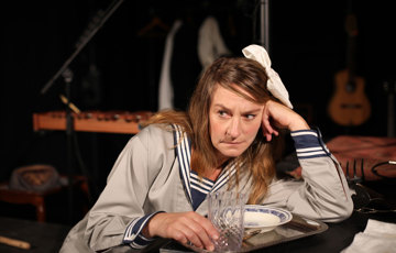 En flicka med rosett i håret och sjömanskostym hänger på armbågen på en bordsskiva.