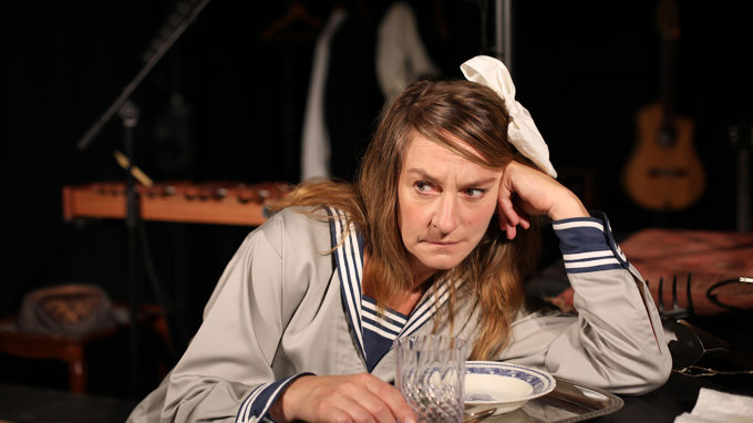 En flicka med rosett i håret och sjömanskostym hänger på armbågen på en bordsskiva.