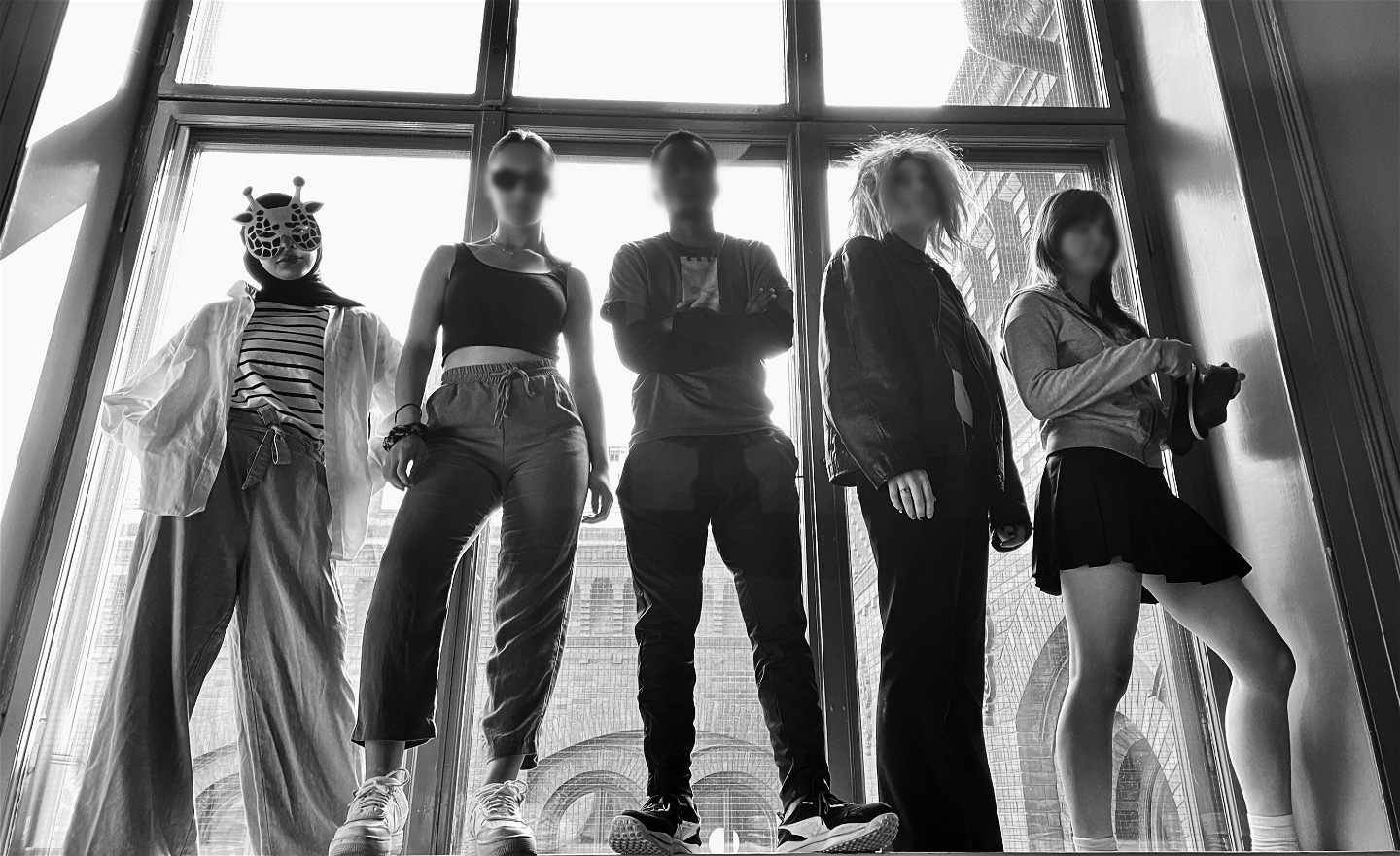 Fem ungdomar står högt upp i ett stort fönster. Det är motljus och de syns som silhuetter. De ser bestämda och tuffa ut.