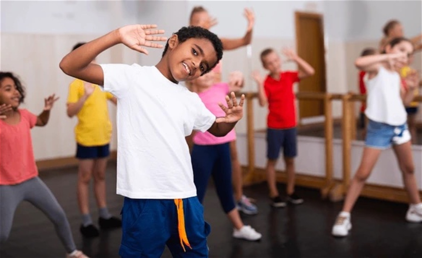 En mångsidig grupp barn står med fötterna brett isär, överkropparna lätt böjda åt ena sidan och händerna som inramar deras leende ansikten.