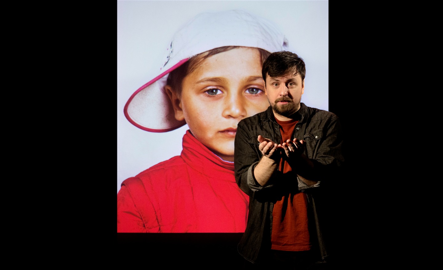 Skådespelare står framför fotografi av liten pojke i keps.