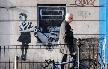 Ett foto på en grafittimålning på en vägg. Motivet är en en bankomat med klor som fångar in en liten flicka.