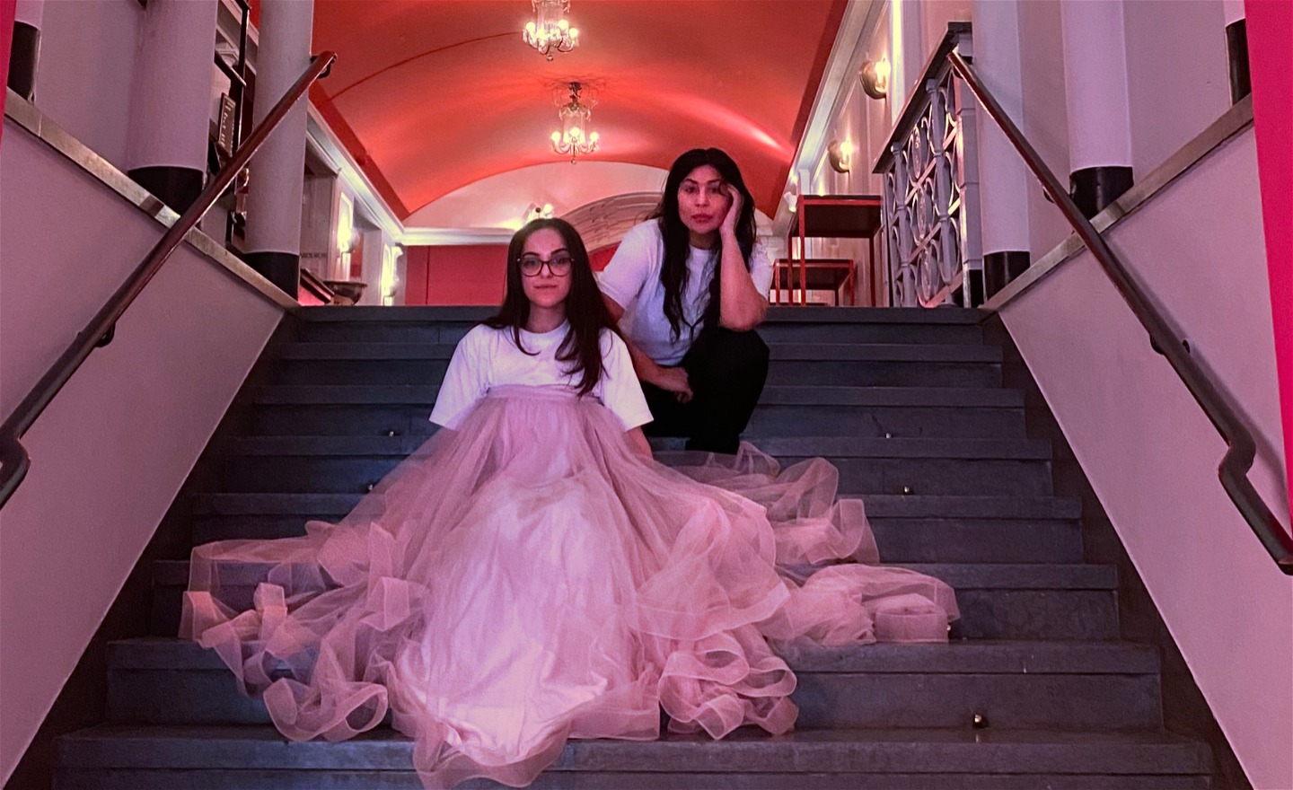 Skådespelaren Nina Rashid bär en stor rosa kjol, sittandes i Folkoperans foajétrappa tillsammans med regissören Bahar Pars. 