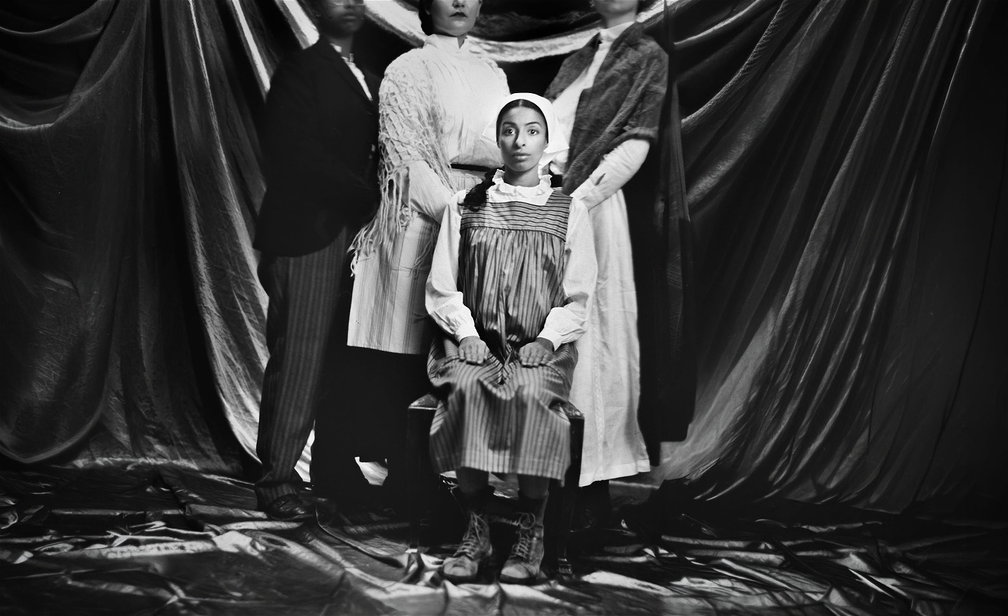 Svartvit gammaldags bild som föreställer ett familjefoto med en spänd ung kvinna i fronten.