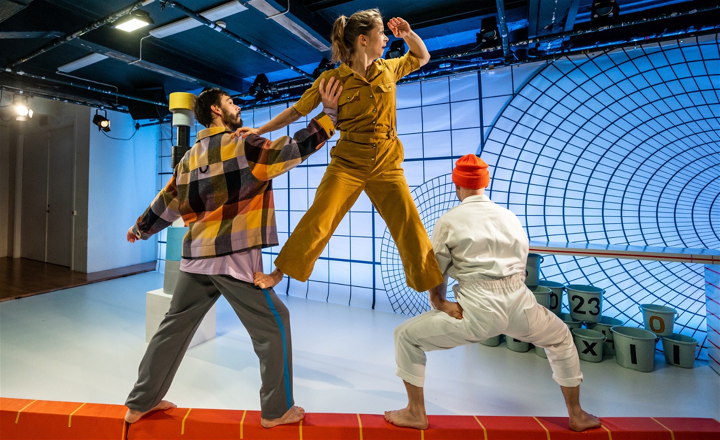 Tre dansare gör en pyramid samtidigt som dom balanserar på en tallinje. 