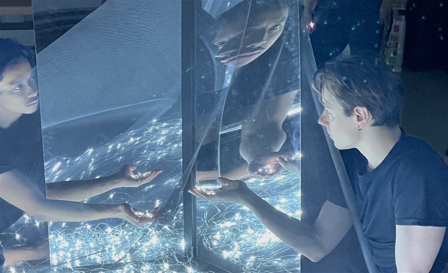 Två män sträcker  sina händer med lysande kulor framför speglar så ansikten och händer fördubblas