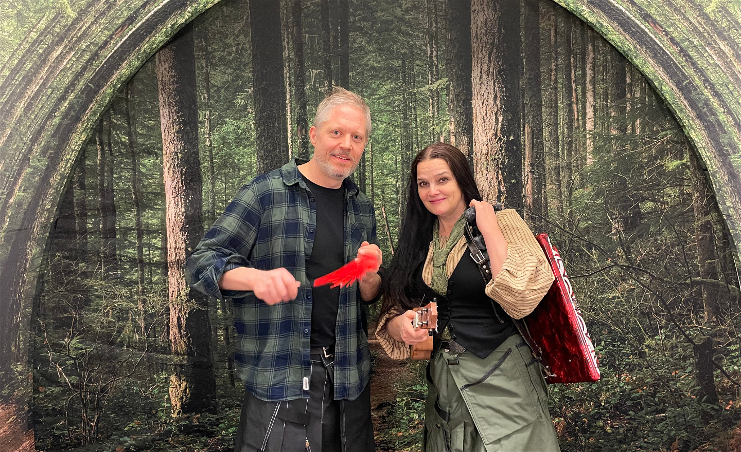 Två skådespelare med instrument framför en granskog