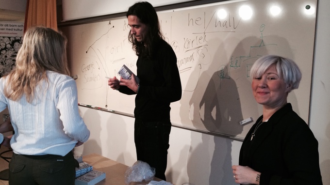 Tre personer framför en skrivtavla fylld med anteckningar i ett klassrum. 