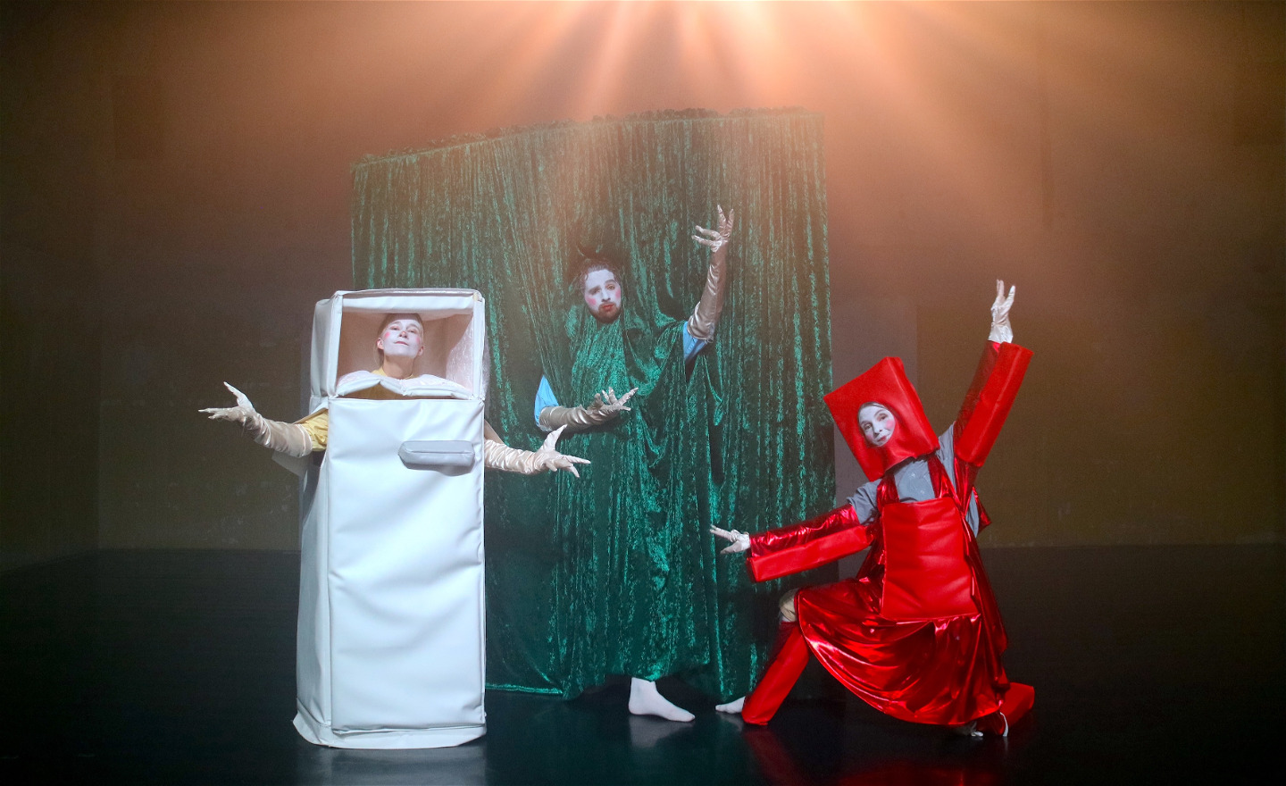 Tre figurer på scenen utklädda till vitt kylskåp, grön gardin och röd stol