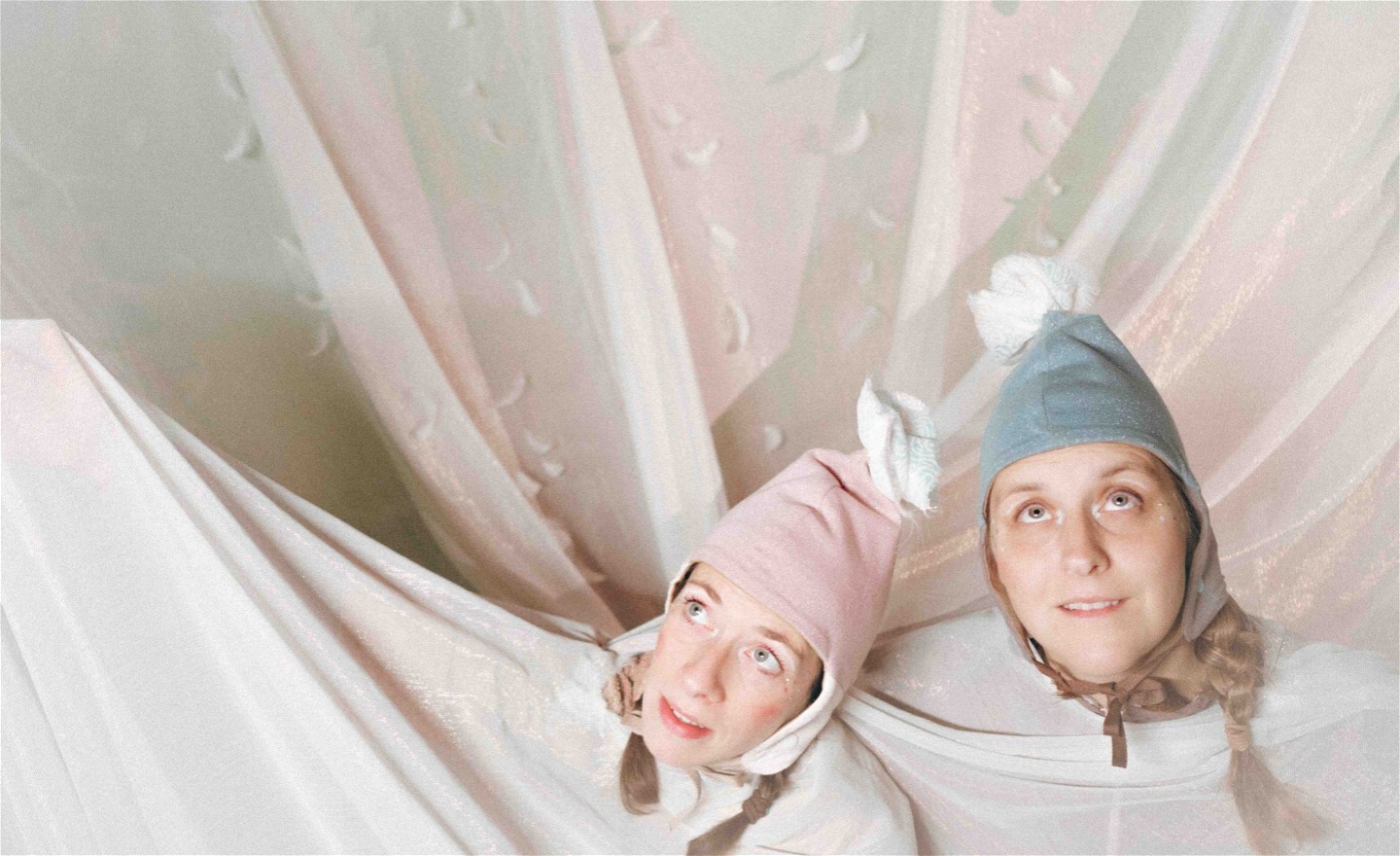 Två kvinnliga scenaktörer sitter i ett hav av vita tunna tyger. 