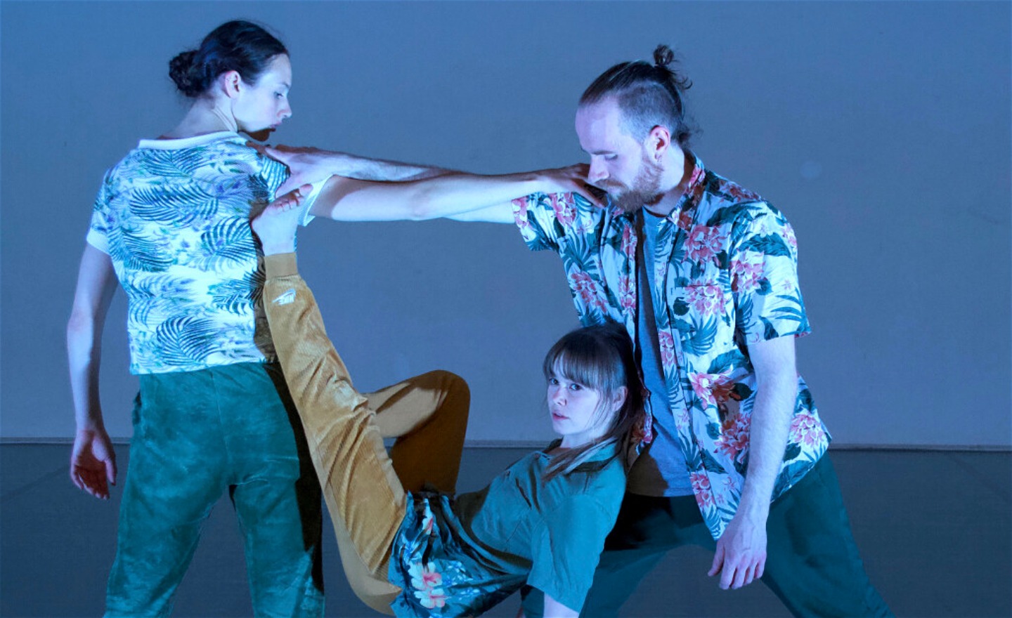 Två dansare med sammnflätade armar och en tredje dansare som ligger mot den enas knä med benen mot den andras rygg.